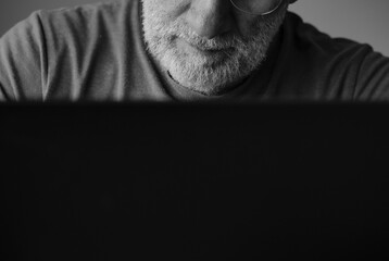 Monochrome of adult man with glasses using laptop in room