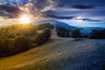 green pasture on the hillside at twilight. day and night time change concept. forested mountains in...