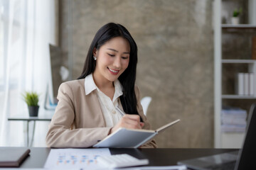 Beautiful Asian woman sitting in the office using a laptop .Happy business woman smiling and enjoying work.