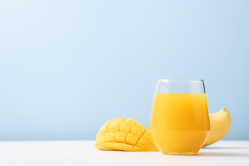 Mango juice in glass and sliced mango fruit on blue background. Tropical fruit juice concept