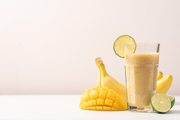 Banana mango smoothie in a tall glass on a light background. Diet breakfast. Tropical fruit drink...