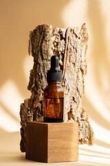 Serum in an amber glass bottle with dropper lid on wooden 3d podium against piece of tree bark....