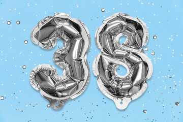 Silver foil balloon number, digit thirty eight on a blue background with sequins. Birthday greeting card with inscription 38. Top view. Numerical digit. Celebration event, template.