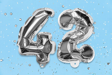 Silver foil balloon number, digit forty two on a blue background with sequins. Birthday greeting...
