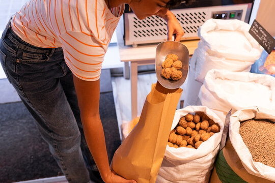 Crop woman packing walnuts into paper bag