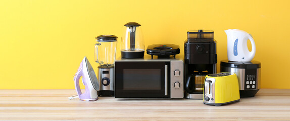 Different household appliances on table against yellow background