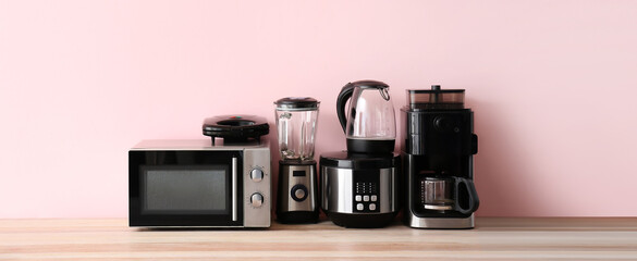 Different household appliances on table against pink background - obrazy, fototapety, plakaty