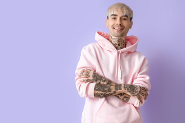 Fototapeta na wymiar Young tattooed man in pink hoodie on lilac background