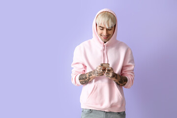Naklejka premium Young tattooed man in pink hoodie using mobile phone on lilac background