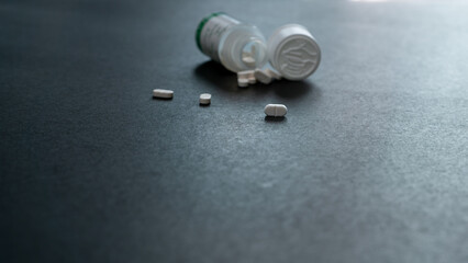 White tablets pills and blur plastic pill bottle on dark floor. Prescription drugs. Pharmaceutical...