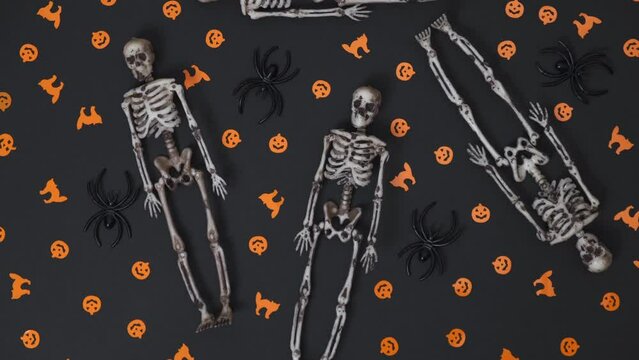flat creative composition of Halloween decorations and randomly lying decorative human skeletons rotates on an orange background. Halloween concept. flat lay, top view, space for text. 4k.