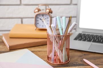 Fototapeta na wymiar Metal cup with pens and pencils on table near white brick wall, closeup