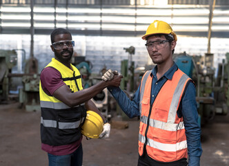 African engineer man and male Asian engineer holding hands to encourage eacher for successful teamwork in industrial factory, Engineer concept