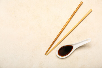 Spoon of soy sauce and chopsticks on light background