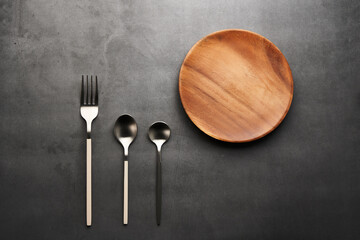 暗いグレーの机の上で整列したスプーンとフォークと木の皿