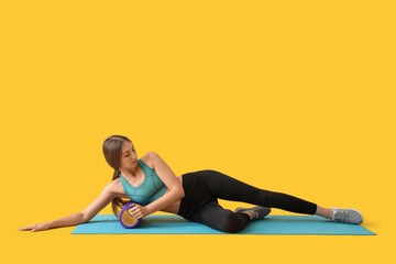 Young woman training with purple foam roller on yellow background