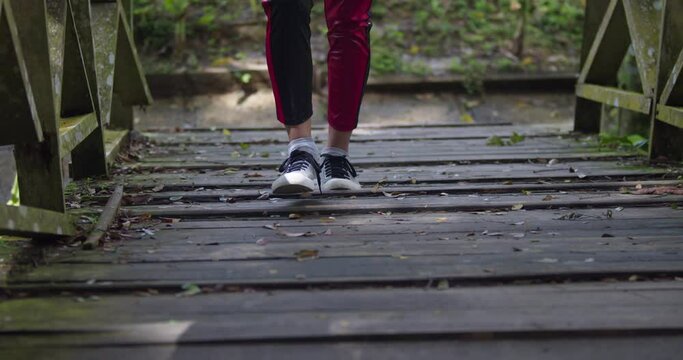 Feet walking on a wooden bridge in grey sneakers