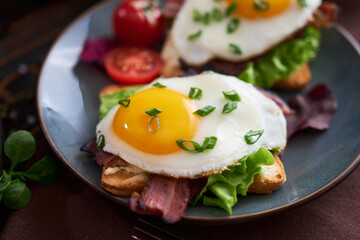Tasty breakfast - fried egg toasts, bacon, tomatoes on wooden kitchen table
