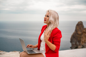 Fototapeta na wymiar A woman is typing on a laptop keyboard on a terrace with a beautiful sea view. Freelancing, digital nomad, travel and vacation concept.