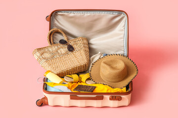 Suitcase with clothes, beach accessories and passport on pink background
