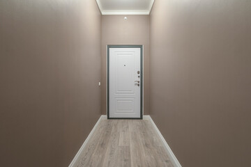 An empty long narrow corridor with laminate flooring, beige walls and a white door.