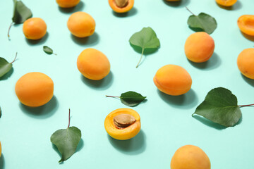 Many ripe apricots and green leaves on color background