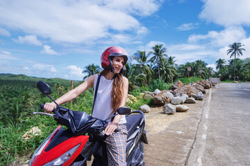 Tropical travel and transport. Young beautiful woman in helmet riding scooter on the road with palm trees. © luengo_ua