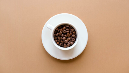 A cup of coffee with a saucer and coffee beans on a brown solid background