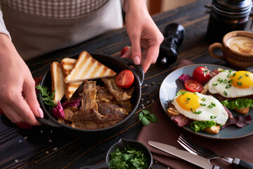 Tasty breakfast - fried egg toasts, bacon, tomatoes on wooden kitchen table