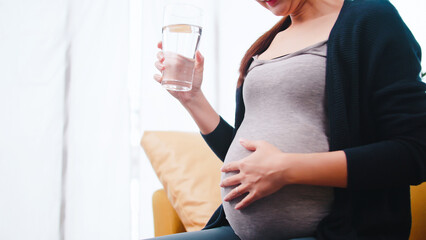 Asian pregnant woman drinking water on the sofa at home.