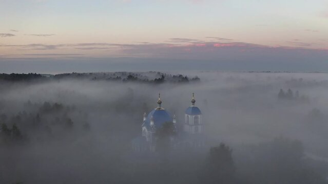 Luftaufnahme einer orthodoxen Kirche im Nebel vor Sonnenaufgang.