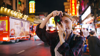 A female tourist enjoys taking photos of the night view of Yaowarat Road or Chinatown in Bangkok, Thailand.