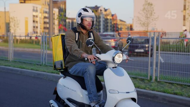 A courier rides a scooter on the road in sunny weather. City delivery service
