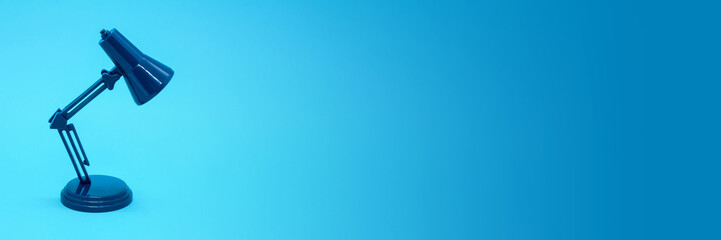 Miniature desk lamp of dark blue color on bright blue background. Space for text. Concept: education, training, session, courses. Banner with free space for text.