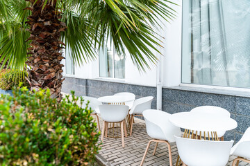 Street cafe with white chairs, green foliage around. Without people, tourism, travel.