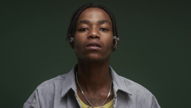 A young stylish black man, preparing himself, looking down the camera, in front of a green background