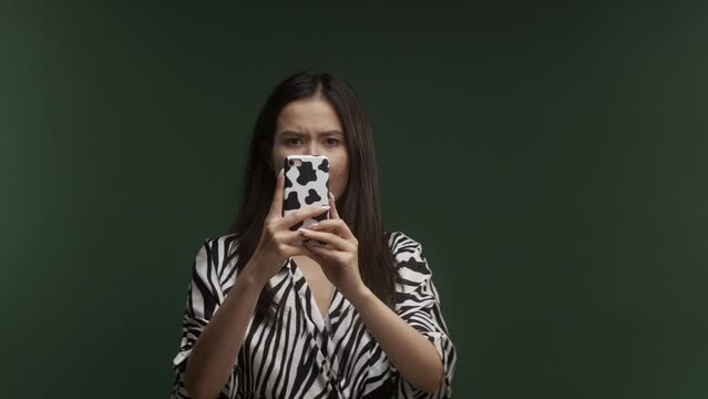A young Asian woman, wearing a zebra pattern dress, taking photographs with her cow print phone, getting a good picture, in front of a green background