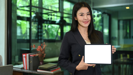 Gorgeous millennial businesswoman showing digital tablet with white display and smiling at camera