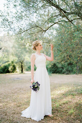 Bride with a bouquet of flowers stands near an olive tree
