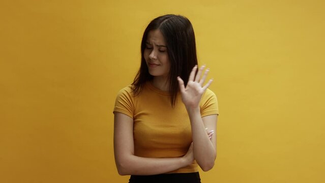 A young asian woman on a yellow background wagging her finger, saying no, disagreeing 