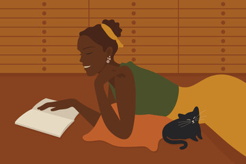 Young Black woman lying on her stomach and reading book in quiet space, living room, study or library. Relaxing, cozy, warm mood. Enjoying literature.
