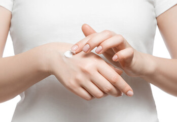 Cropped shot of a woman in white t-shirt applying hand cream, isolated on white. Well-groomed short natural nails.