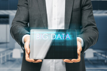 Close up of business man hand holding tablet with creative digital text hologram on blurry office interior background. Information, technology and big data concept.