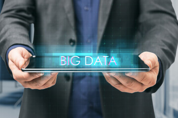 Close up of man hand holding tablet with creative digital text hologram on blurry office interior background. Information, technology and big data concept.