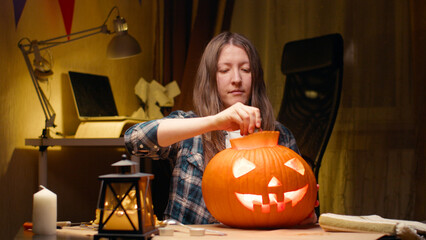 Cutting into pumpkin and taking lid with seeds out. Halloween preparations. Woman sitting and carving with knife halloween Jack O Lantern pumpkin at home for her family.