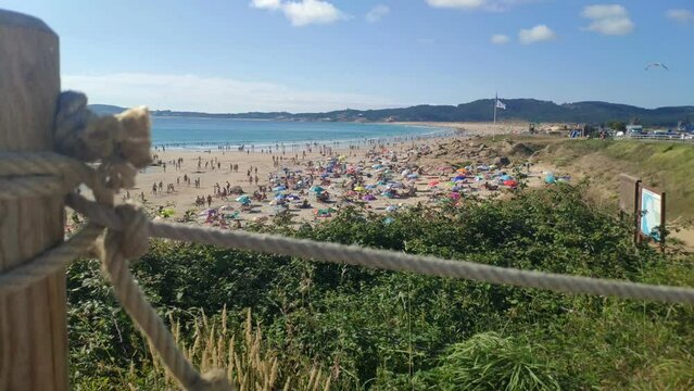 people enjoying a sunny summer day on the beach in the hot afternoon. A seagull approaches by flying slowly descending from the sky. Panoramic shot. A Lanzada, Pontevedra, Spain