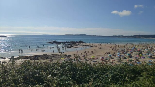 people enjoying a sunny summer day on the beach on the hot afternoon with the blue sky. Panoramic shot. A Lanzada, Pontevedra, Spain