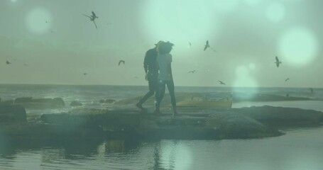 Animation of light spots over biracial couple at beach - Powered by Adobe