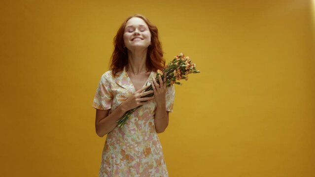 A young ginger white woman surprised and catching a bouquet of flowers in front of a yellow background