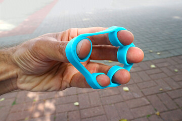 A person shakes his fingers and muscles of the hand with a reverse expander. Shallow depth of field.